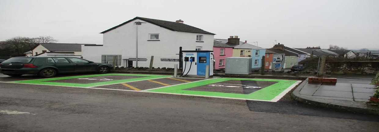 2 green electric charge points in a carpark at Edde cross with colourful houses in the background