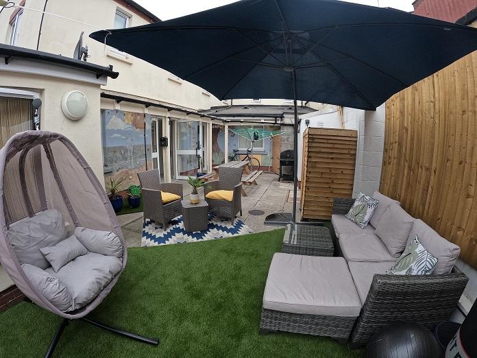 Outside area of odyssey house with swinging chair, comfy sofas, large parasol and dining area