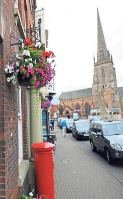 image of street in Hereford with St peters Church in background and a red pillar box to the forefront with cars parked