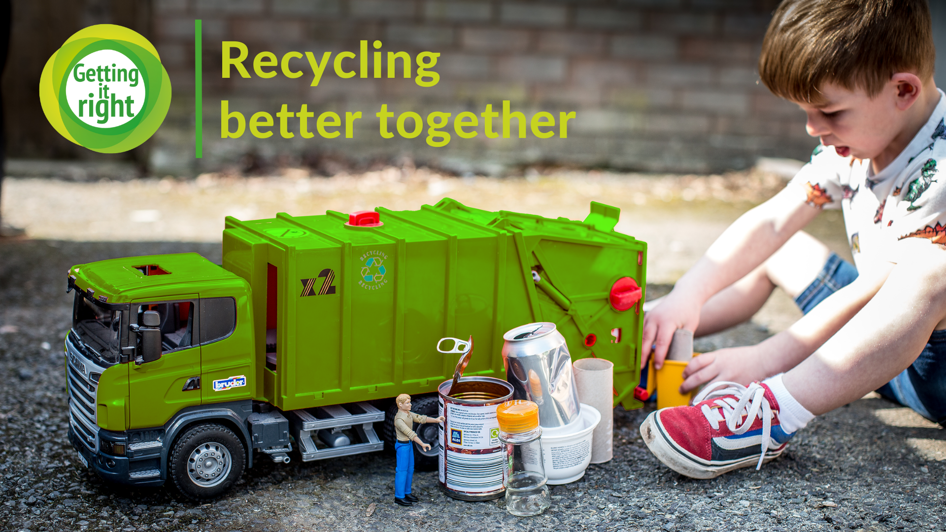 Child plays with toy rubbish lorry alongside some items to be recycled