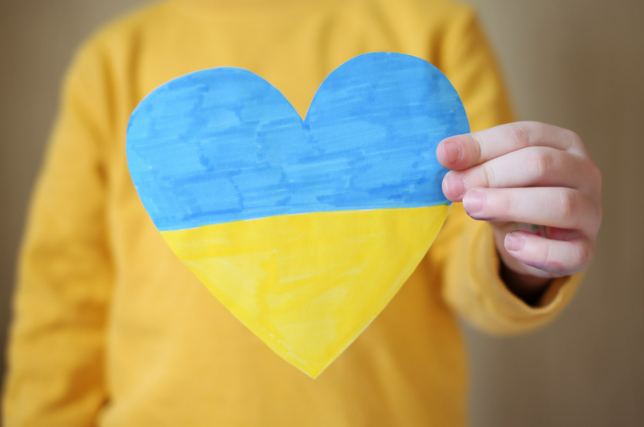 Person in yellow top holding heart made from paper with blue and yellow stripes, representing Ukraine