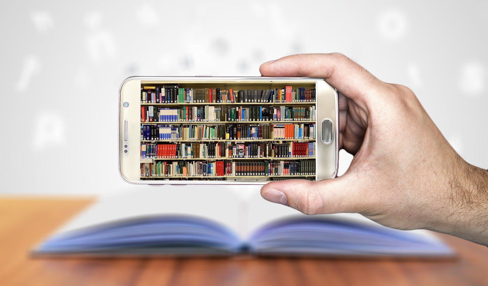 Person&#039;s hand holding a mobile phone with a picture of a library of books on